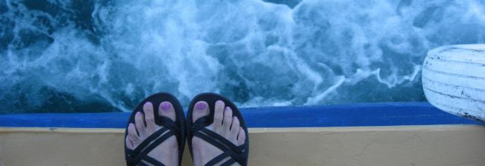 Womans feet in sandles on the edge of a ferry boat with frothy foam traveling over the water